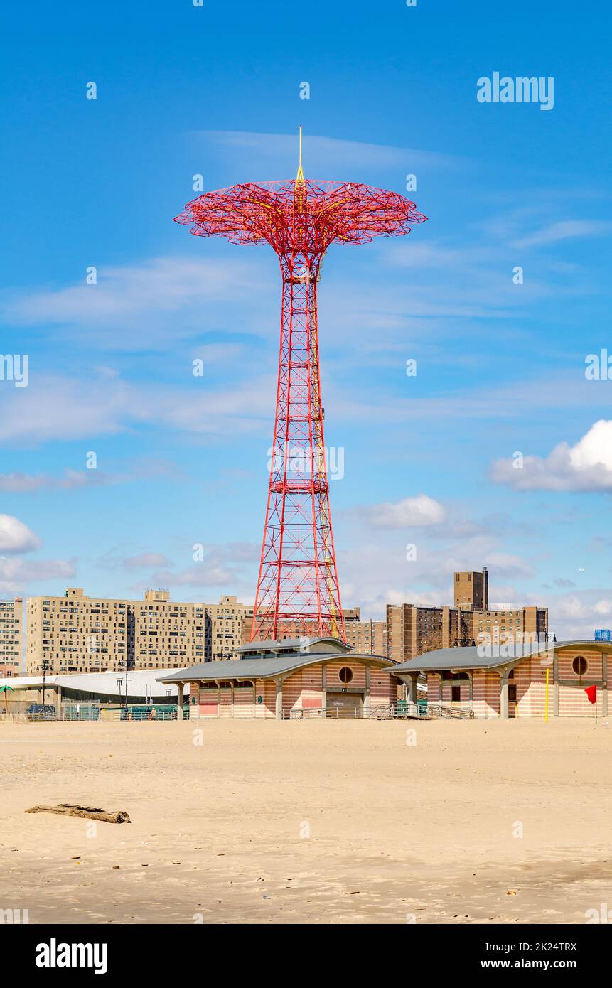 Red Parachute Jump al Luna Park Amusement Park, Coney Island, Brooklyn con la spiaggia vuota e gli edifici di fronte durante la soleggiata giornata invernale con il cielo nuvoloso Foto Stock