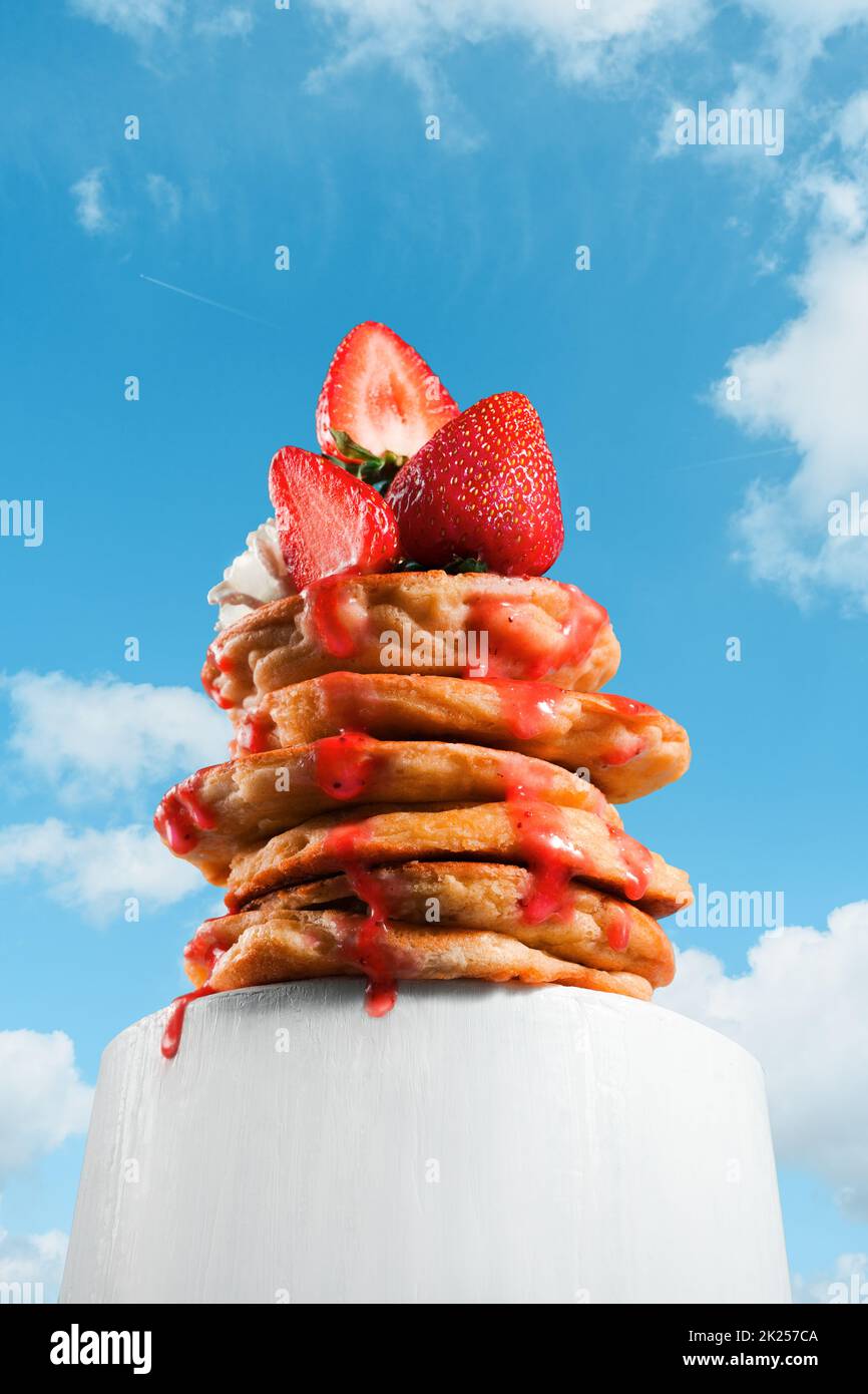 Pila di frittelle o torre di frittelle sparate dal basso, effetto prospettiva. Pacchetto creativo di frittelle con frutti di bosco, fragole e dripp appetitoso Foto Stock
