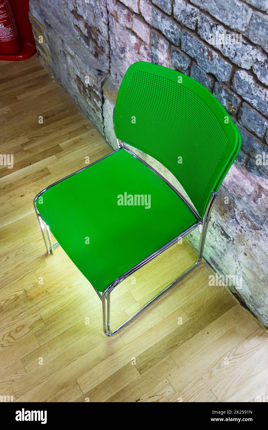 Una sedia di plastica verde su un pavimento di legno da una parete di mattoni, illuminata da sotto Foto Stock