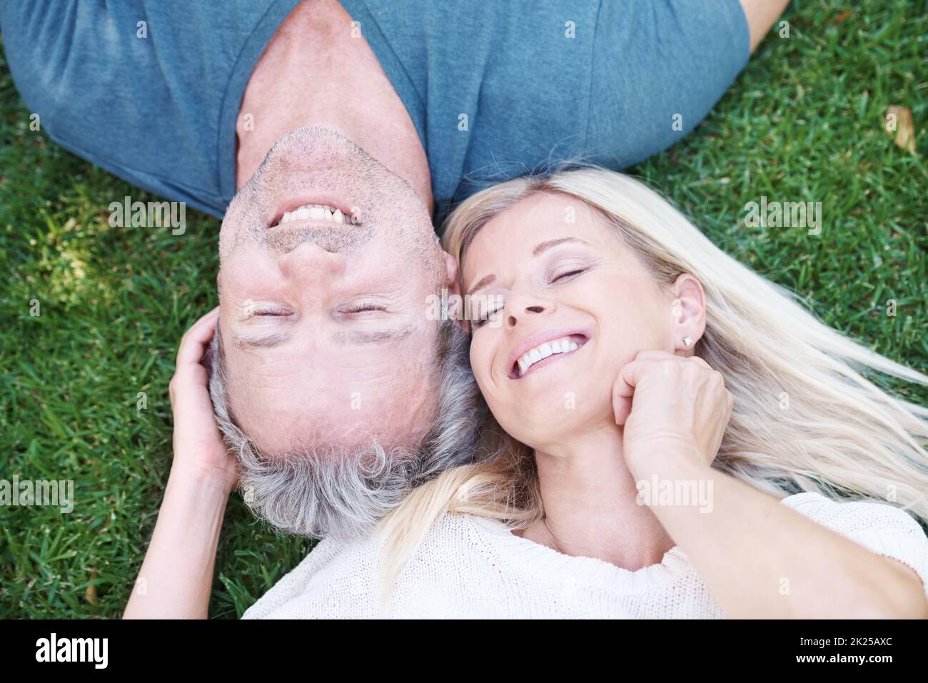 Questo è semplicemente superlativo. Una coppia matura sdraiata sull'erba sorridendo con gli occhi chiusi. Foto Stock