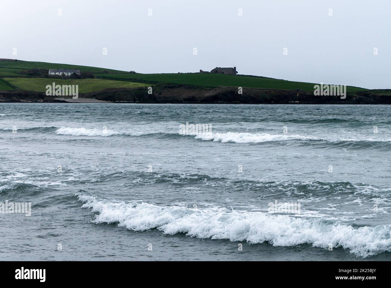 Onde di mare in alta marea. Un edificio su una collina sulla riva del mare. Cielo grigio cupo, edificio su verde prato vicino al mare. Paesaggio marino, schiuma bianca o Foto Stock