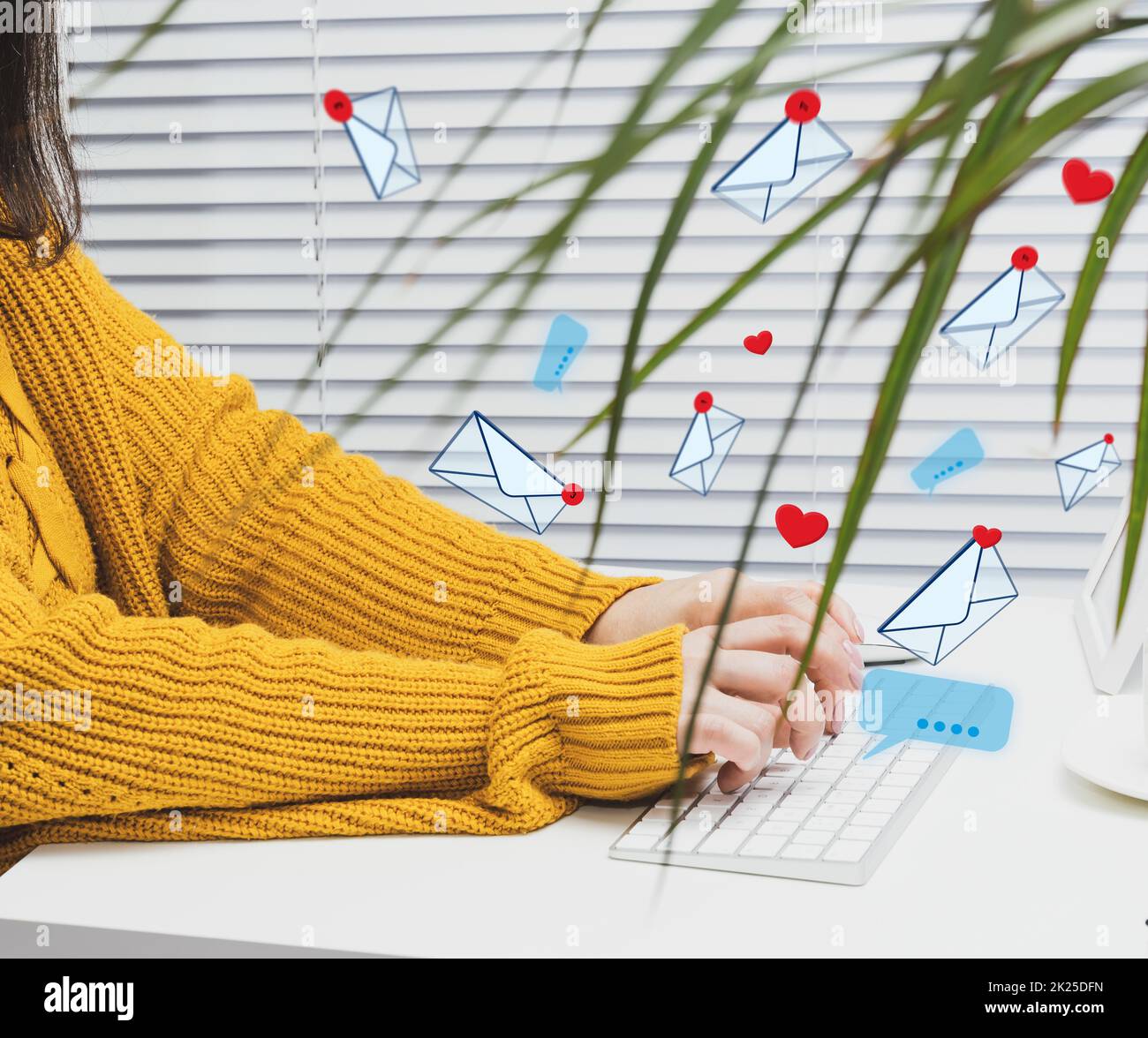 una donna si siede a un tavolo bianco e digita su una tastiera wireless, lettere e cuori stanno volando. Dipendenza dai social media, spam e comunicazione online Foto Stock