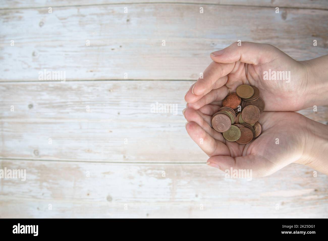 Mani che tengono in mano un mucchio di monete in euro su sfondo di legno. Donazione, risparmio, beneficenza di fondi, concetto di piano di finanza familiare, concetto di crisi finanziaria. Vista dall'alto. spazio di copia Foto Stock