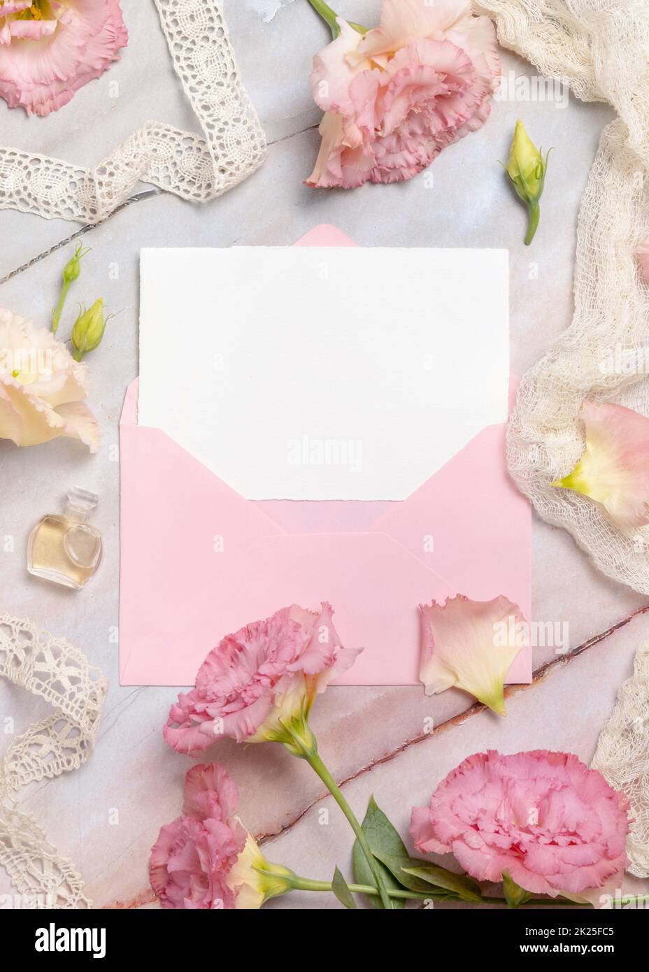 Fiori rosa e una scheda vuota con busta posta su un tavolo di marmo Foto Stock