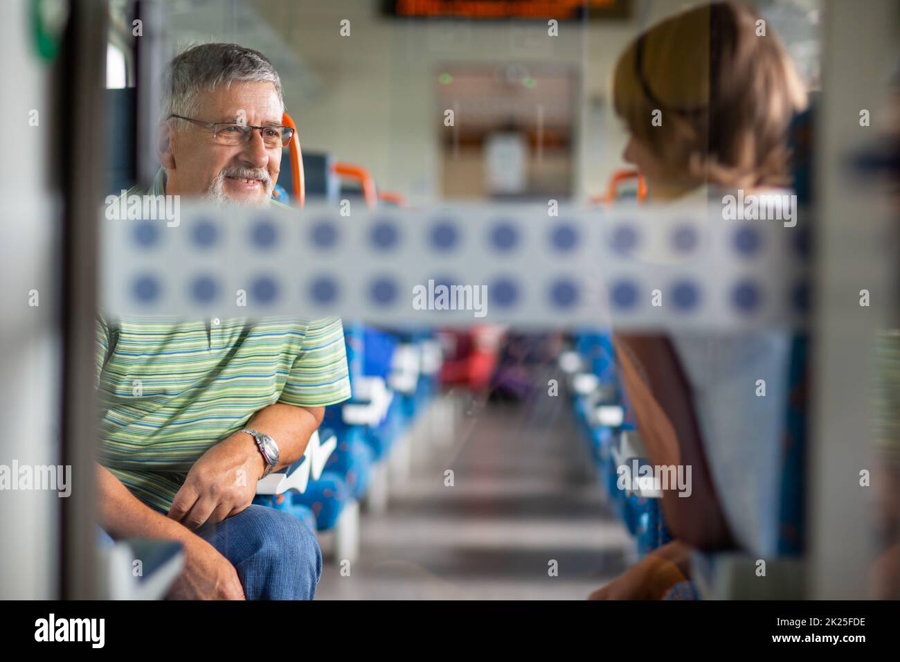 Uomo anziano che si gode di un viaggio in treno - lasciando la sua auto a casa, risparmierà il tempo trascorso viaggiando, parlando con altri passanti a bordo Foto Stock