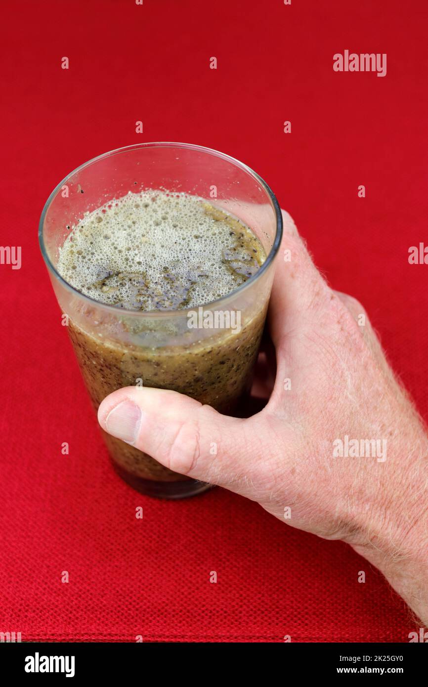 Purea Papaya semi, polpa e acqua in un bicchiere tenuto da una mano Foto Stock