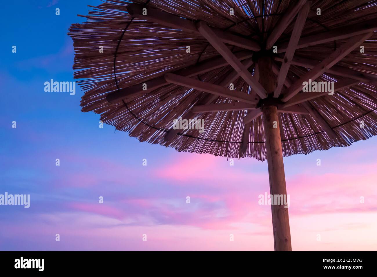 Vista del bellissimo tramonto blu e viola, cielo e ombrellone di paglia Foto Stock