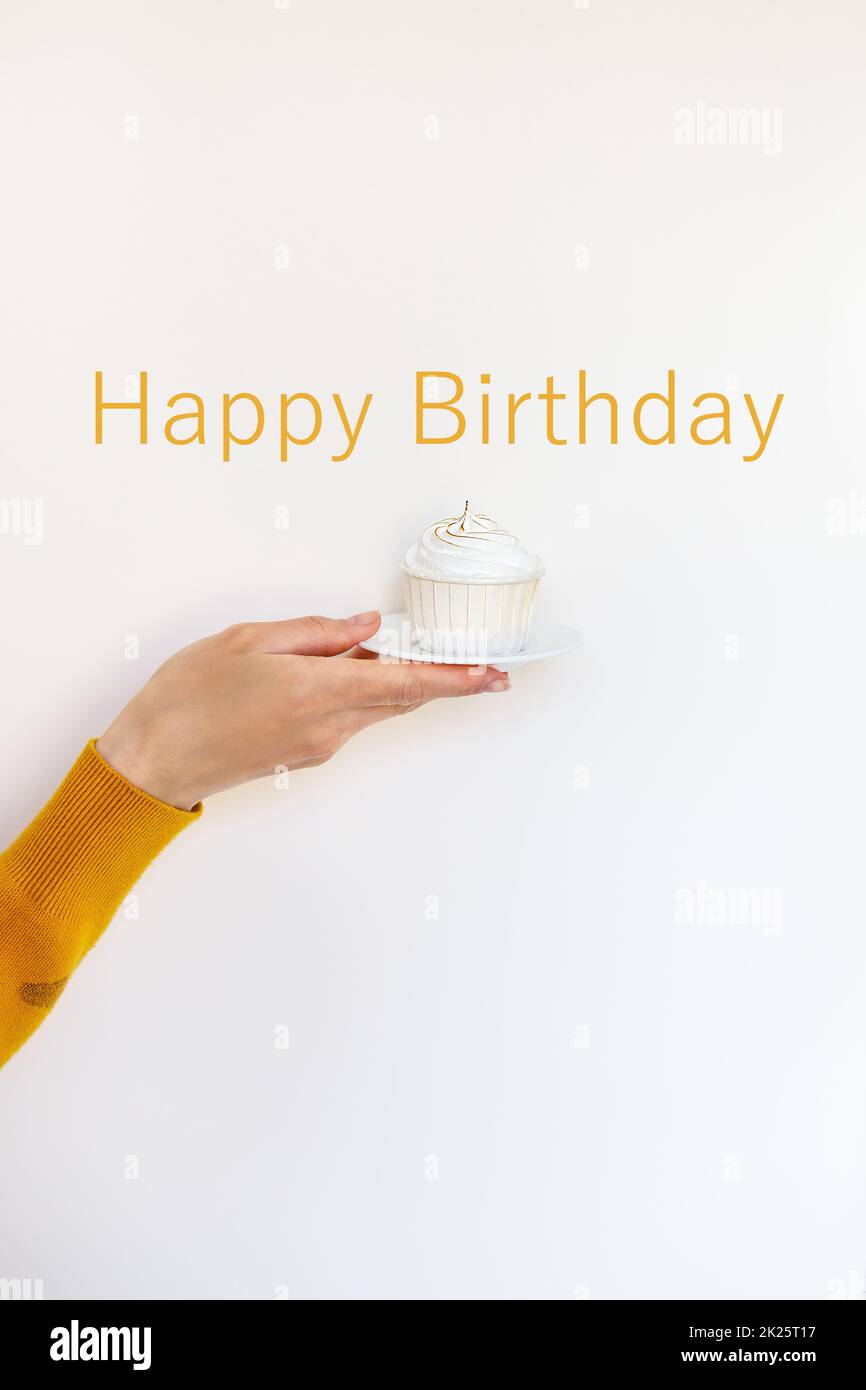 Una mano femminile tiene un delizioso cupcake, congratulazioni per un Buon compleanno. Lettere di buon compleanno. Foto Stock