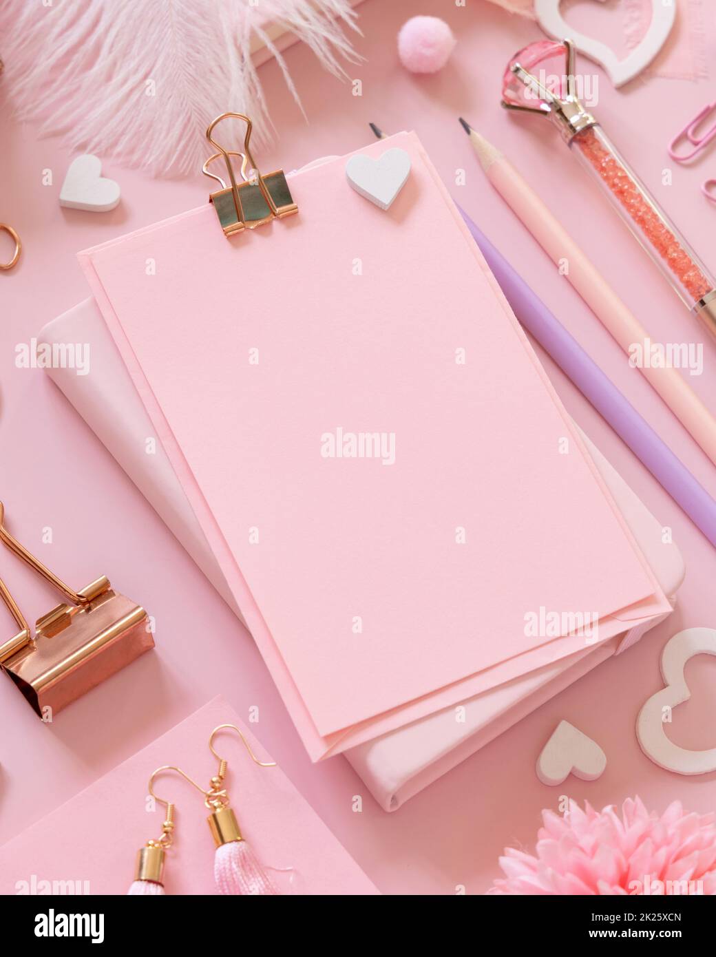 Cartoncino di carta rosa con clip, accessori da scuola girly e cuori su rosa pastello primo piano, mockup Foto Stock