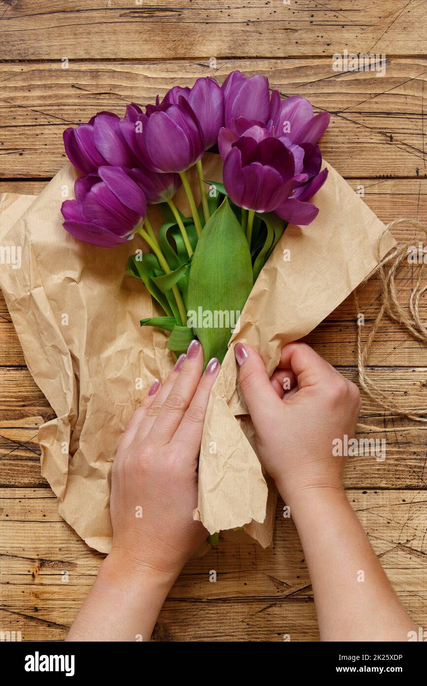 Mani avvolgenti tulipani viola bouquet in carta su tavolo di legno Foto Stock