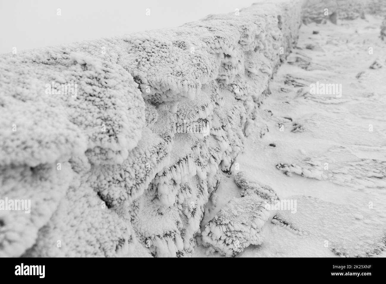 Una recinzione in pietra coperta di ghiaccio e neve. Mettere a fuoco il primo piano. Bianco e nero. Foto Stock