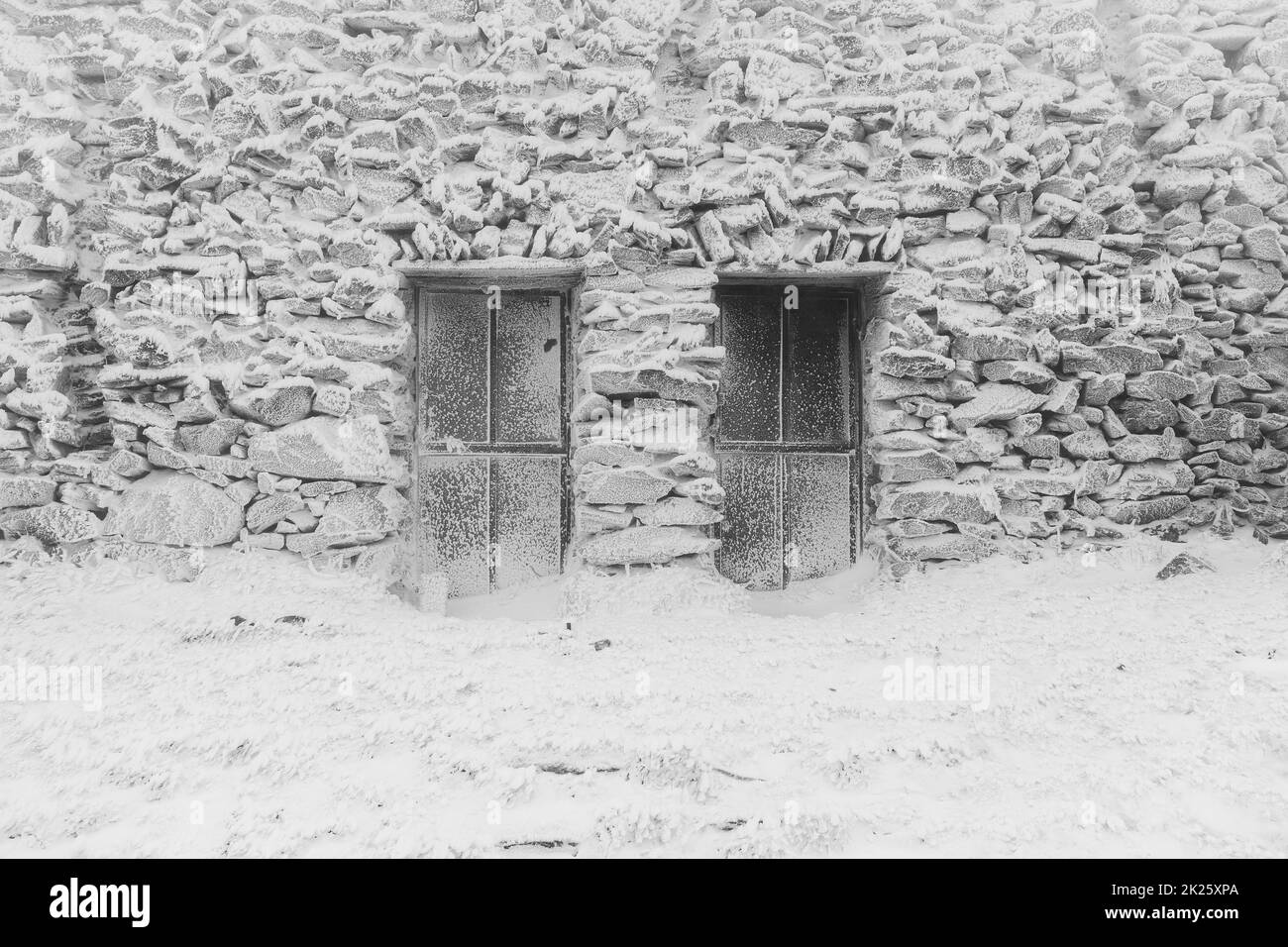 Muro di pietra e finestre di un vecchio edificio abbandonato coperto di ghiaccio e neve. Sfondo. Bianco e nero. Foto Stock