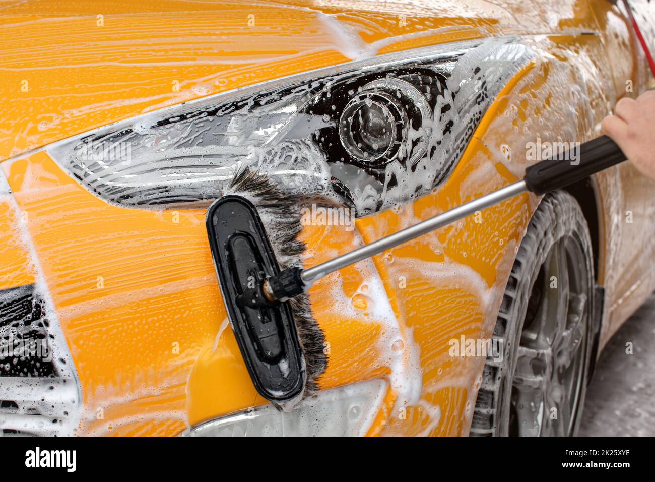 Paraurti anteriore e la luce di un giallo auto lavata in self service autolavaggi, spazzola lasciando tratti bianchi. Foto Stock