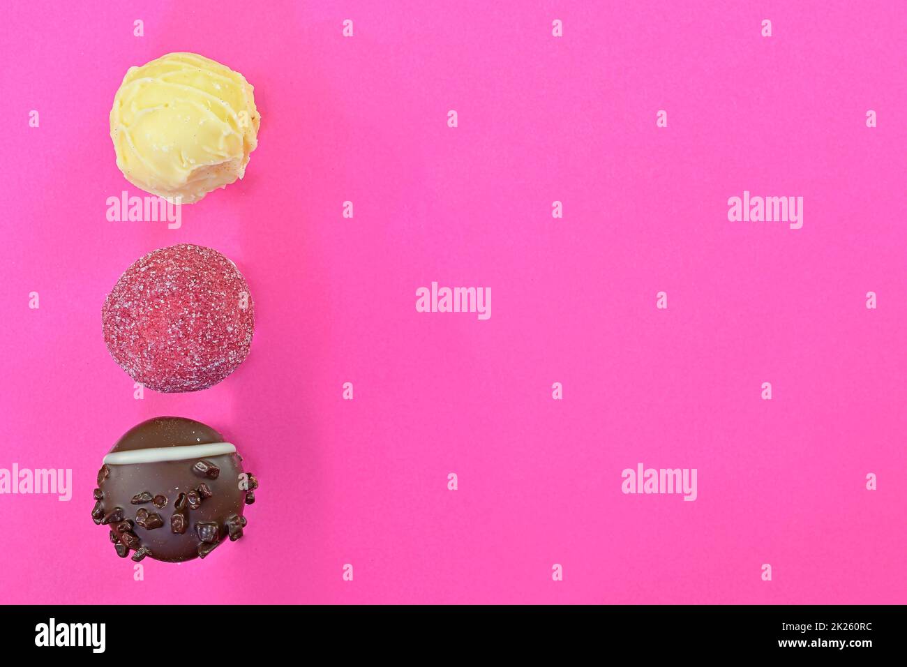 Boni di cioccolato o praline su sfondo rosa. Assortimento di praline al cioccolato su sfondo rosa pastello con spazio per la copia. Disposizione piatta, vista dall'alto Foto Stock