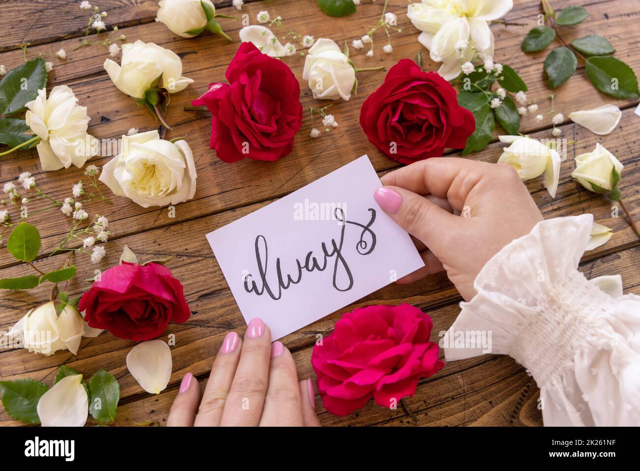 Mani con scheda SEMPRE vicino rosso e fiori crema vicino su un tavolo di legno Foto Stock