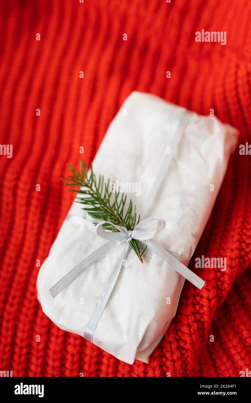 Uno stollen di Natale fatto in casa sigillato in carta bianca del mestiere si trova su un tessuto lavorato a maglia rosso. Confezione regalo. Foto Stock