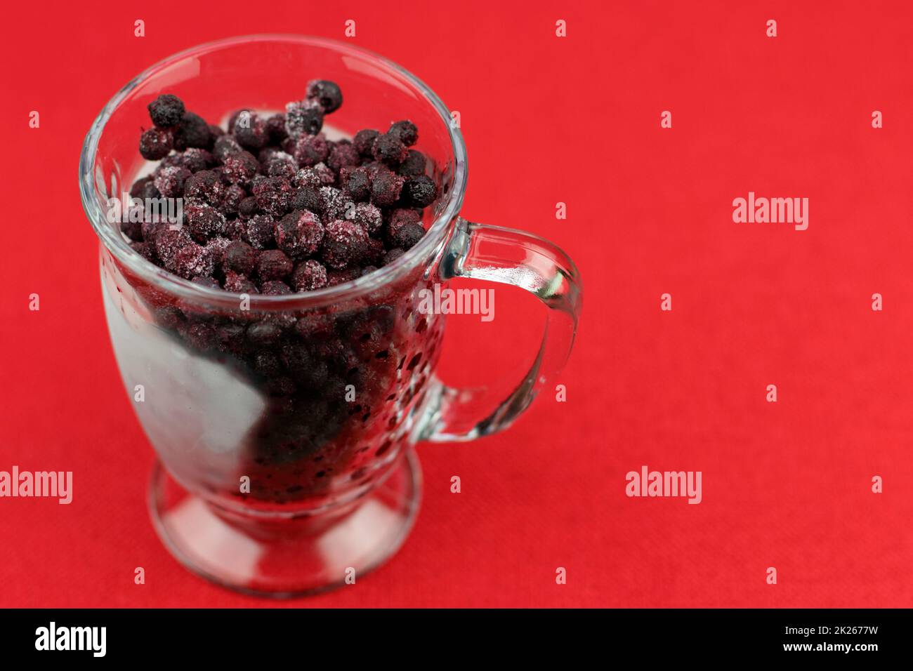 Frutti di bosco congelati in una tazza di vetro primo piano su sfondo rosso Foto Stock