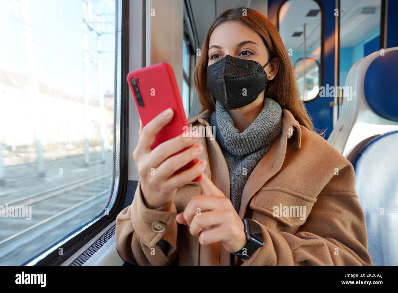 Ragazza in inverno vestiti indossare maschera medica nera sul treno utilizzando il telefono cellulare Foto Stock
