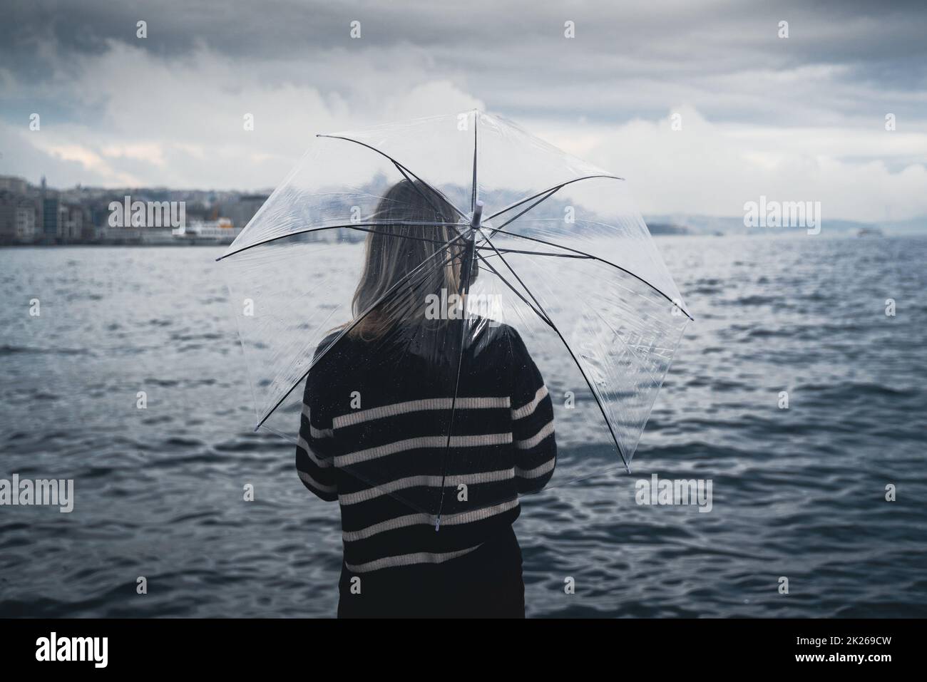 donna che tiene un ombrello trasparente davanti all'acqua Foto Stock