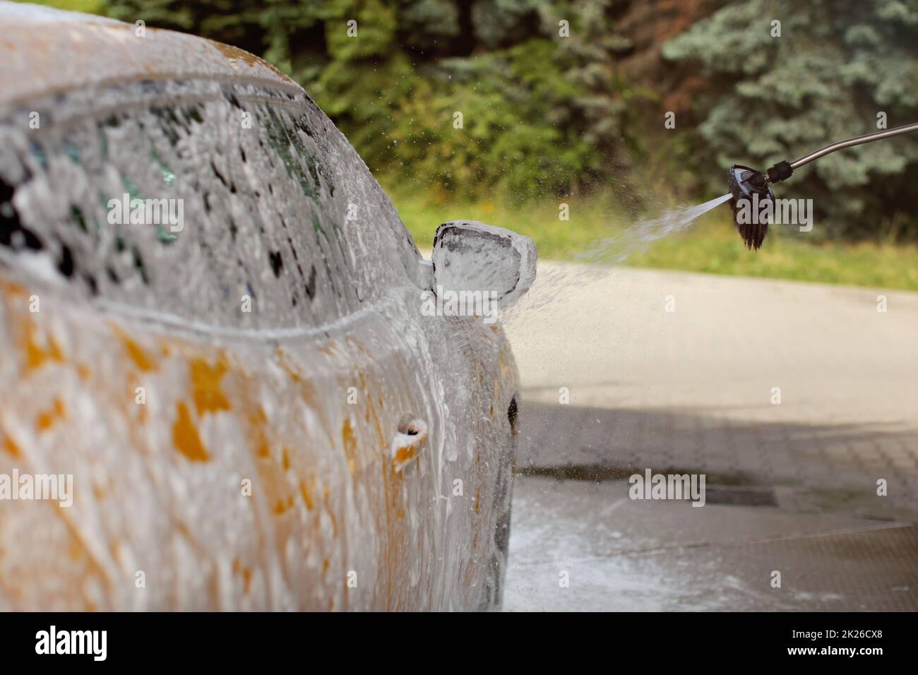 Lato e lo specchietto laterale di giallo auto essendo lavato in self service autolavaggi, schiuma e shampoo spruzzatura, scende nell'aria. Foto Stock