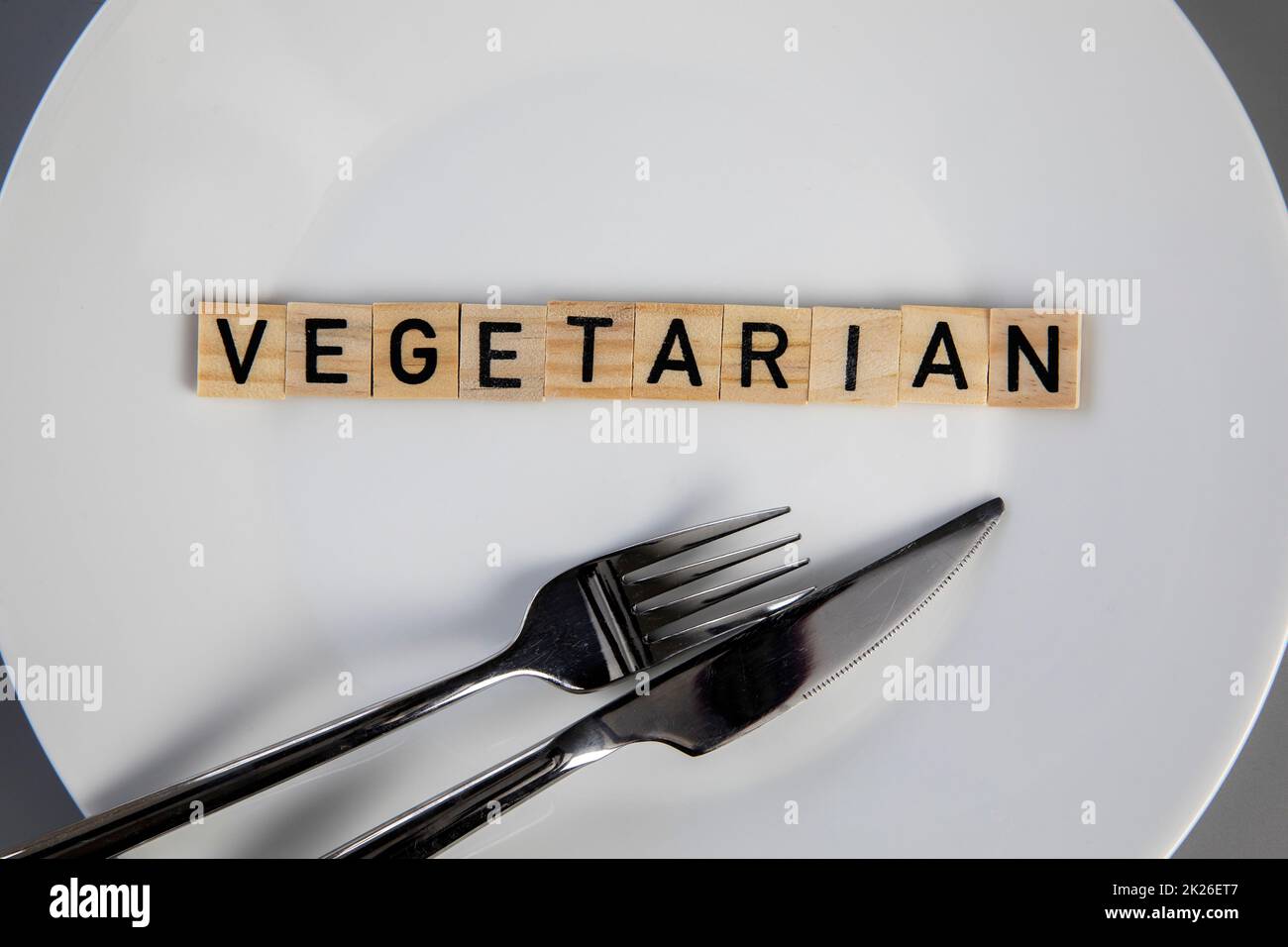 Vista dall'alto piatto bianco con parola vegetariana su sfondo grigio vista dall'alto, coltello e forchetta sul tavolo salute e cibo concetto Foto Stock