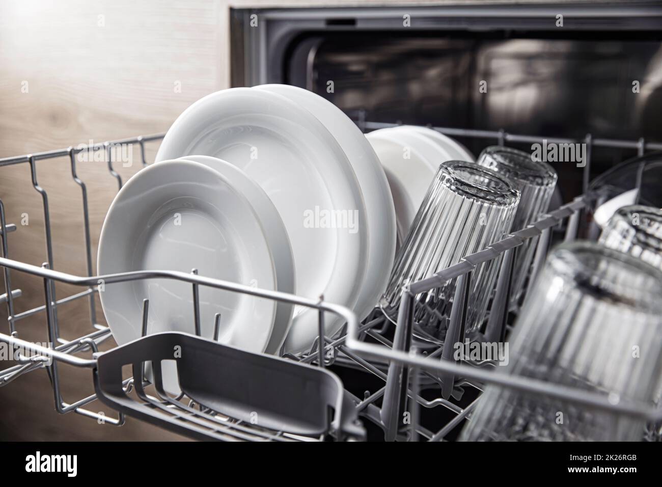 Lavastoviglie aperta con stoviglie pulite all'interno, posate, bicchieri, piatti in cucina Foto Stock