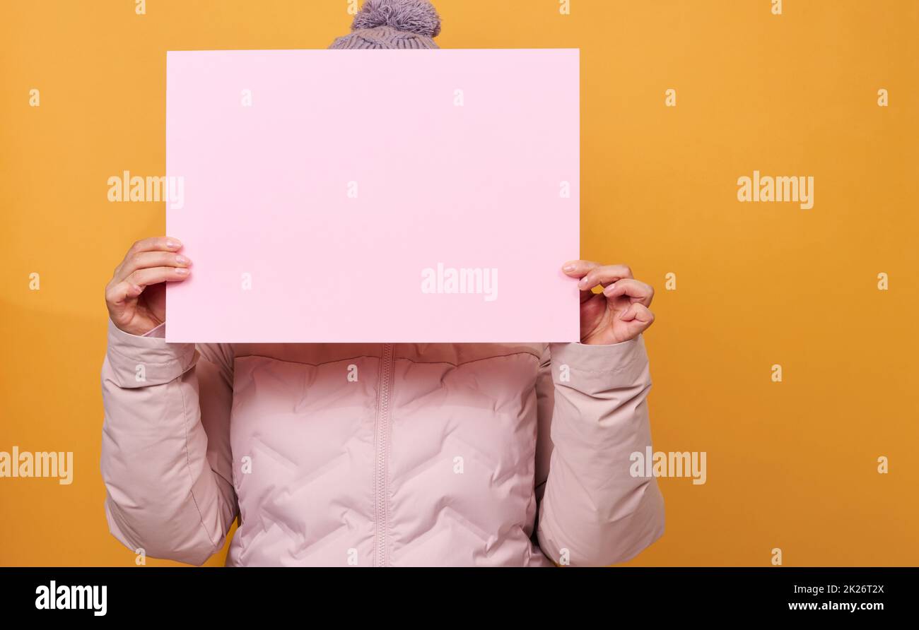 donna in giacca e cappello rosa inverno contiene foglio bianco rosa di carta su sfondo giallo. Vendita stagionale Foto Stock