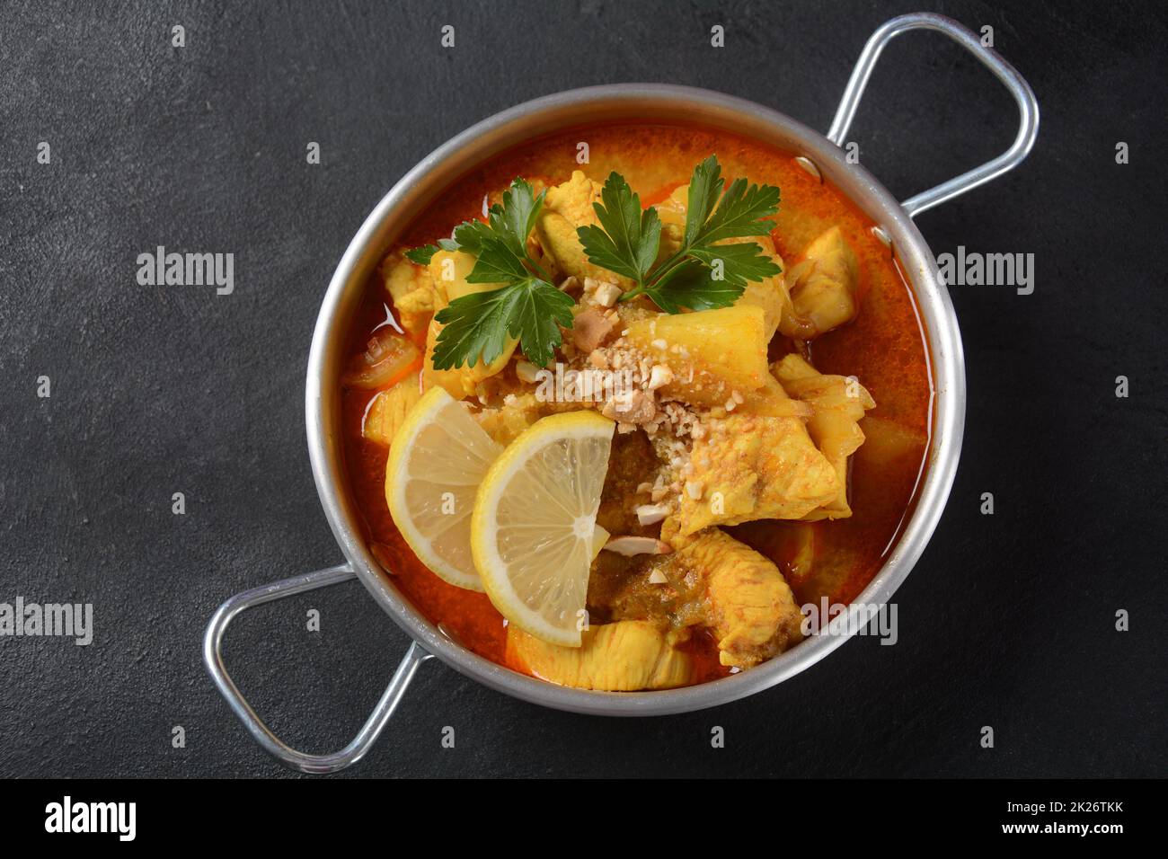 Un curry di Massaman di pollo in ciotola nera su fondo scuro. Il Massaman Curry è il miglior piatto tailandese indiano con carne di pollo, patate, cipolla e molte spezie è influenzato dalle culture musulmane malesi e thailandesi. Foto Stock