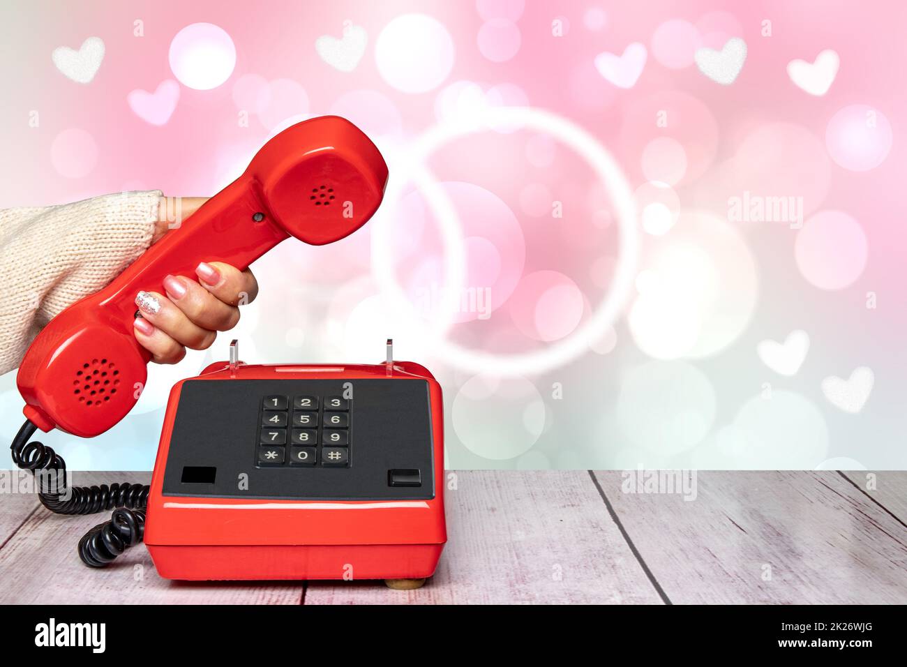 Una donna elegante e femminile splendidamente curata mano che tiene un vecchio telefono cellulare rosso sopra un astratto blurry rosa chiaro San Valentino o sfondo di nozze. Copia spazio. Informazioni generali sulla comunicazione. Foto Stock