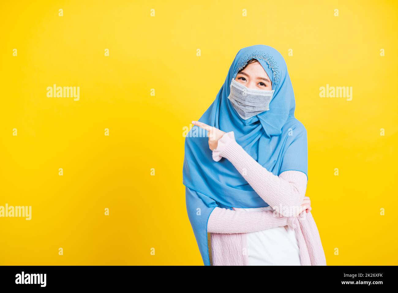 Donna indossare hijab e maschera di protezione del viso per prevenire coronavirus che punta dito lato lontano Foto Stock