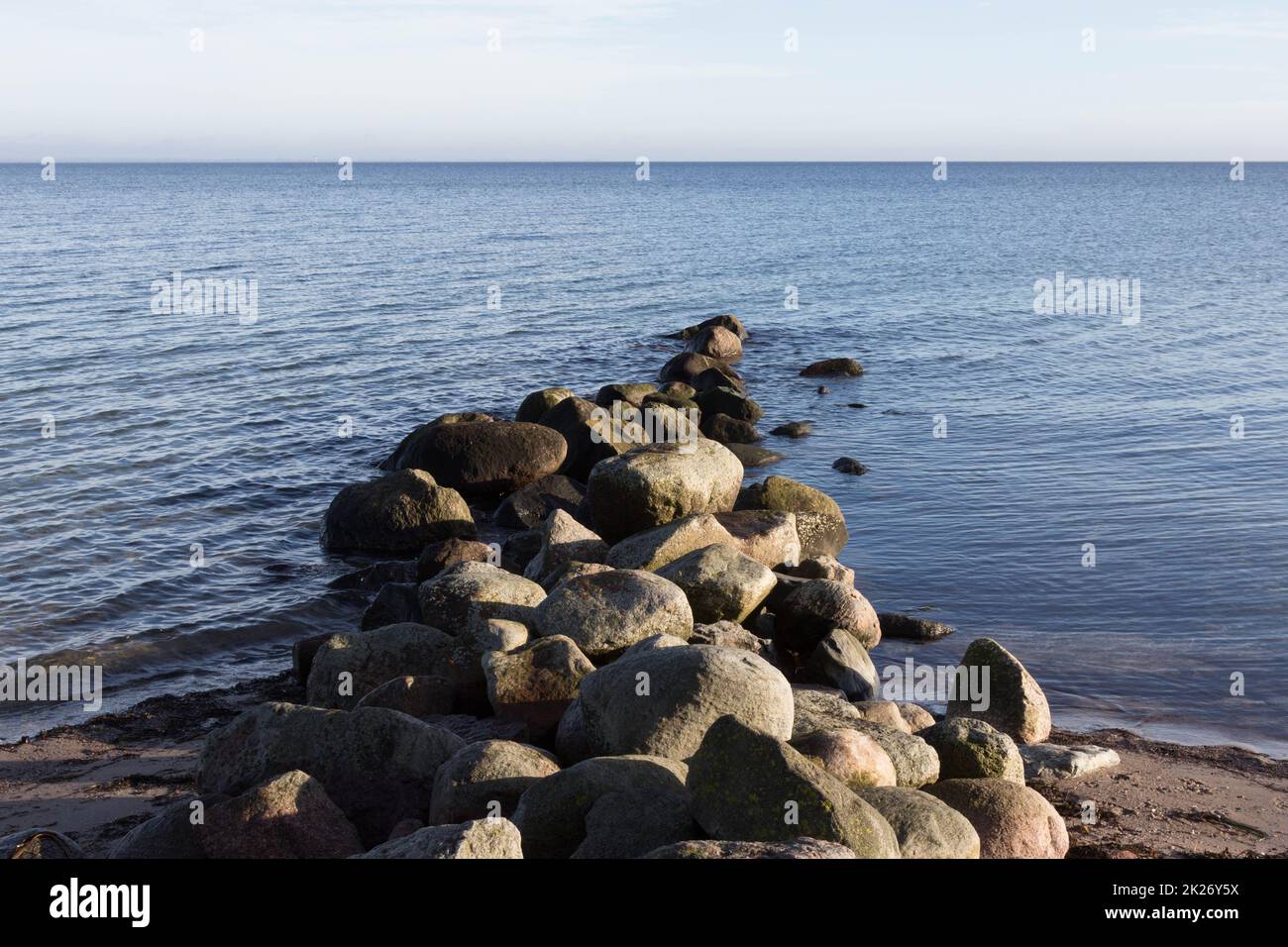 Groyne è fatta di rocce sulla costa del Mar Baltico di fronte ad un orizzonte lontano Foto Stock