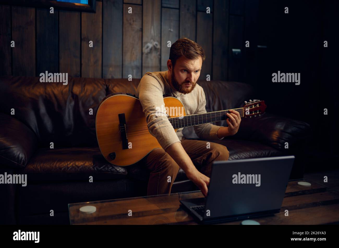 Giovane uomo che impara a suonare la chitarra attraverso internet Foto Stock