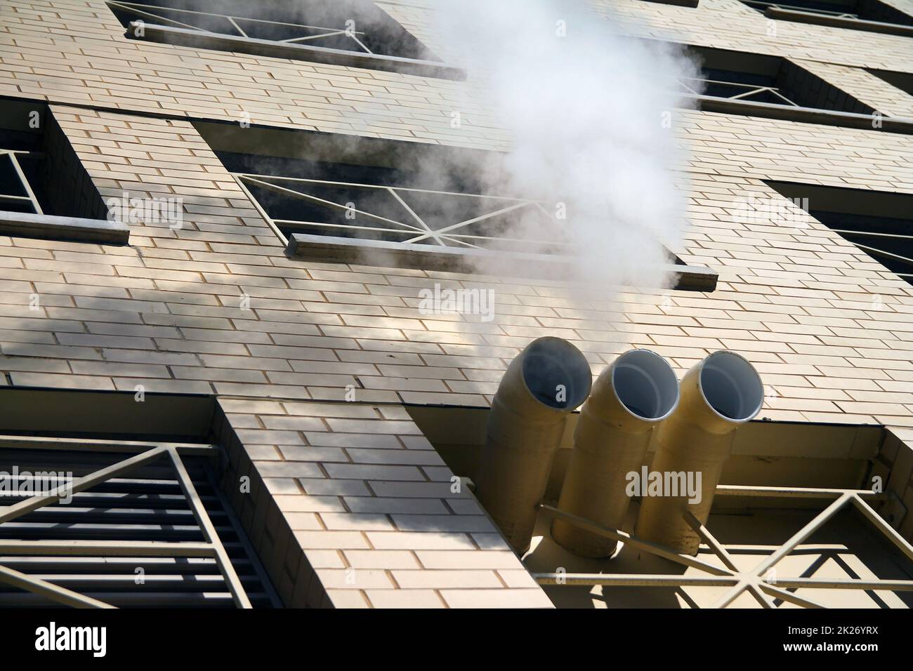 Uno scarico di vapore bianco da tre camini di un edificio in mattoni Foto Stock
