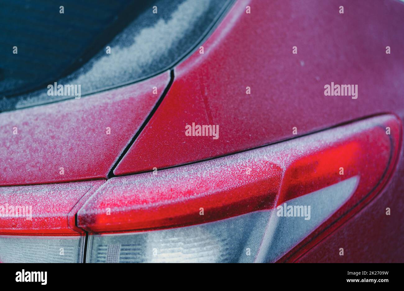 Auto rossa coperta da gelo e ghiaccio di neve bianca nella stagione invernale. Primo piano sul retro dell'auto rossa parcheggiata nel parcheggio esterno. Freddo e gelo. Gelo sul parabrezza posteriore dell'auto e sul fanalino di coda. Foto Stock