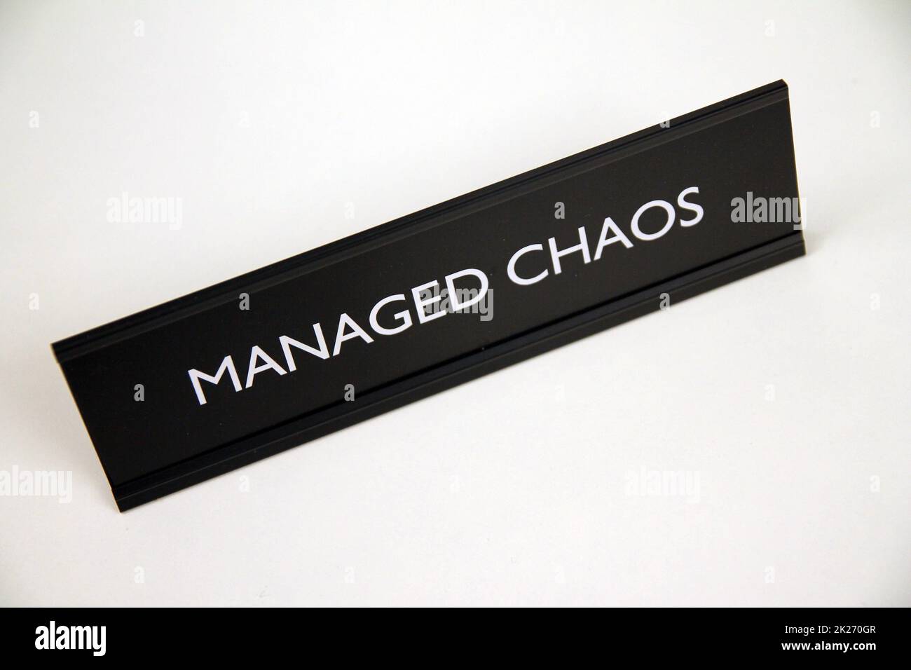 Chaos gestito, metallo nero e argento segno su una mensola bianca Foto Stock