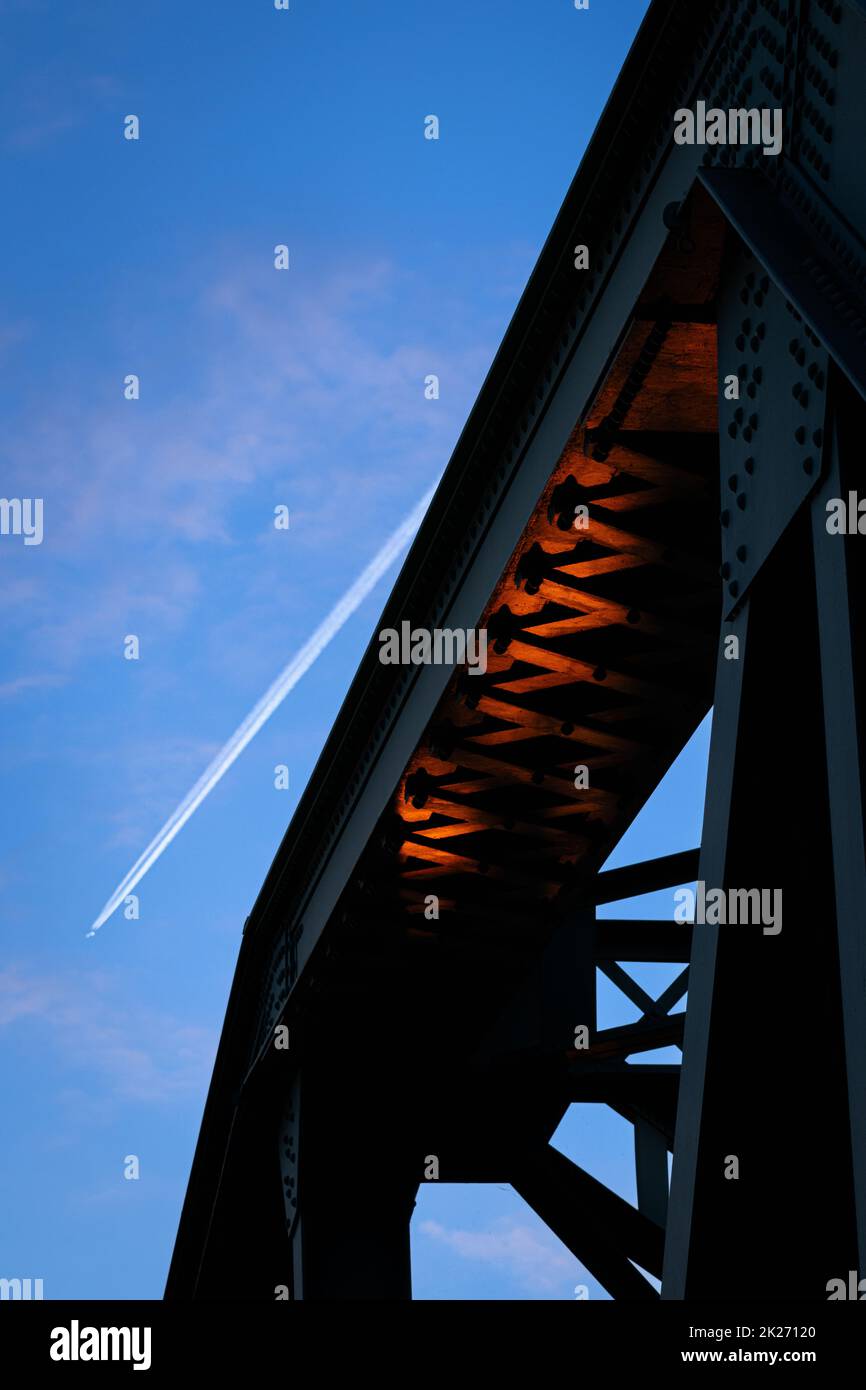 Colonne ponte all'alba, cielo blu sullo sfondo, luce riflessa dal sole e un aereo che passa Foto Stock
