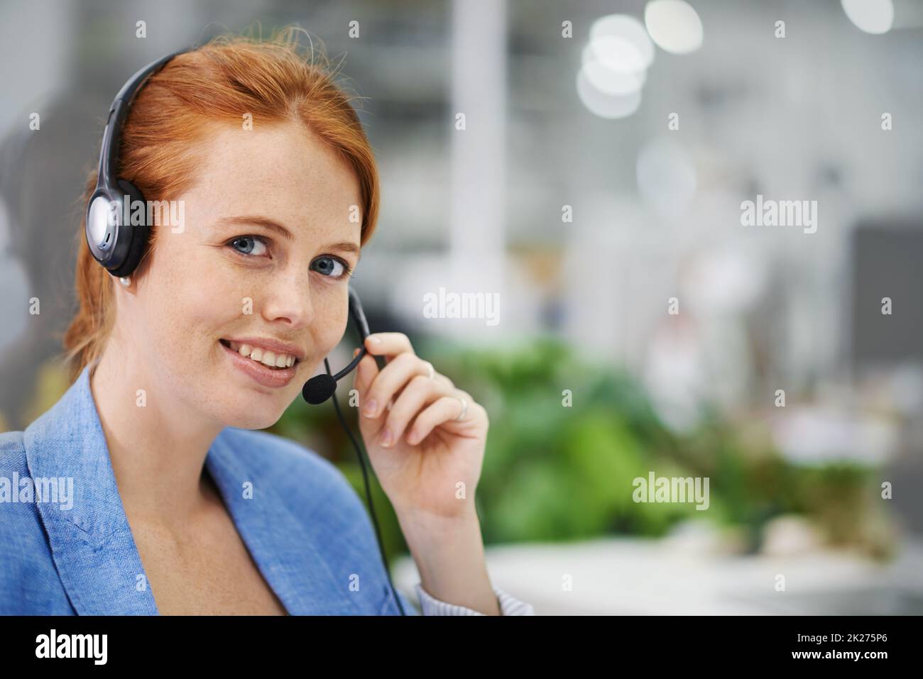 L'assistenza è una telefonata. Shot di un attraente testa rossa indossando set di testa femminile in un ambiente d'ufficio. Foto Stock