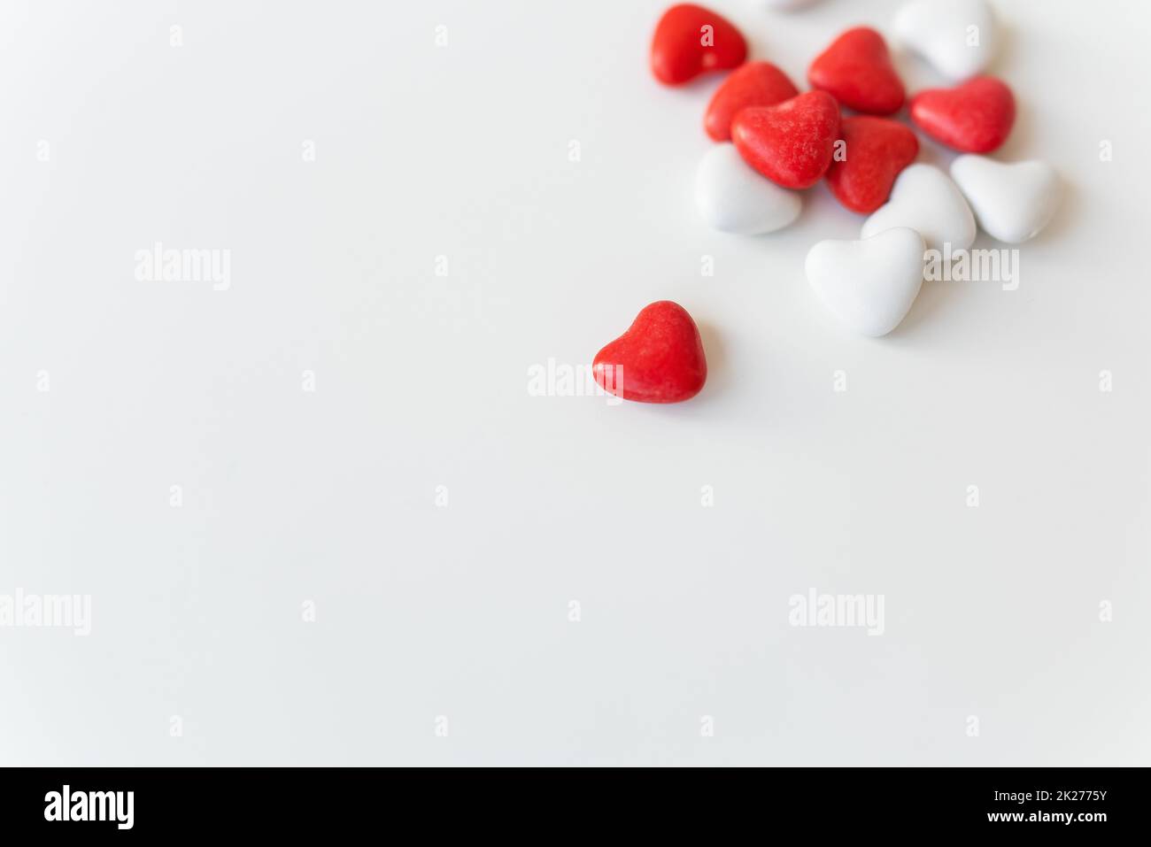 Lo sfondo piatto del giorno di San Valentino si trova sulla parte superiore della vista delle caramelle rosse e bianche a forma di cuore sparse su sfondo bianco. Luogo per un'iscrizione. Foto Stock