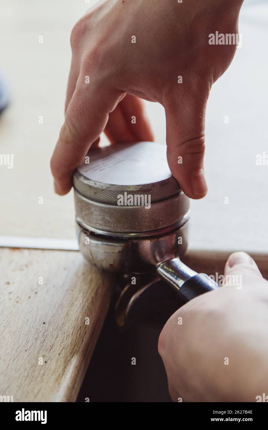 Chiudere il maschio della mano utilizzando un manomissione per premere il caffè macinato in un portafiltro Foto Stock