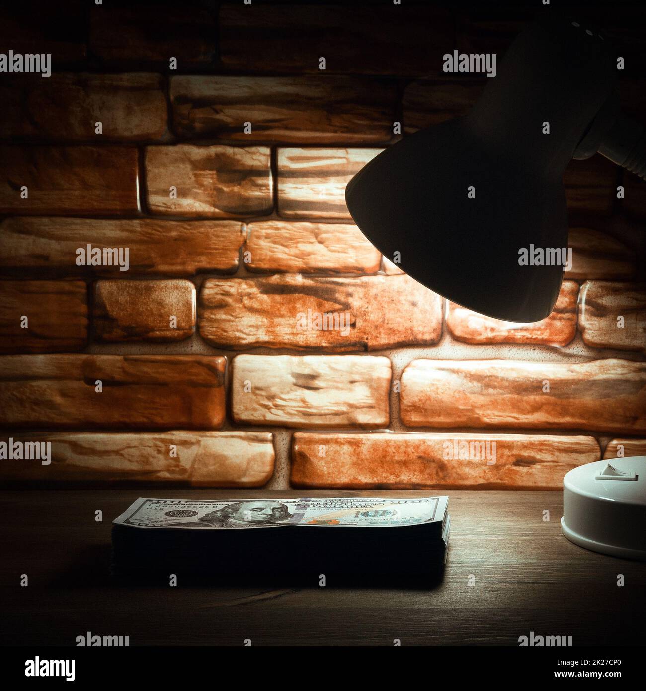 Una pila di banconote da cento dollari su un tavolo di legno è illuminata dalla luce di una lampada sullo sfondo di un muro di mattoni Foto Stock