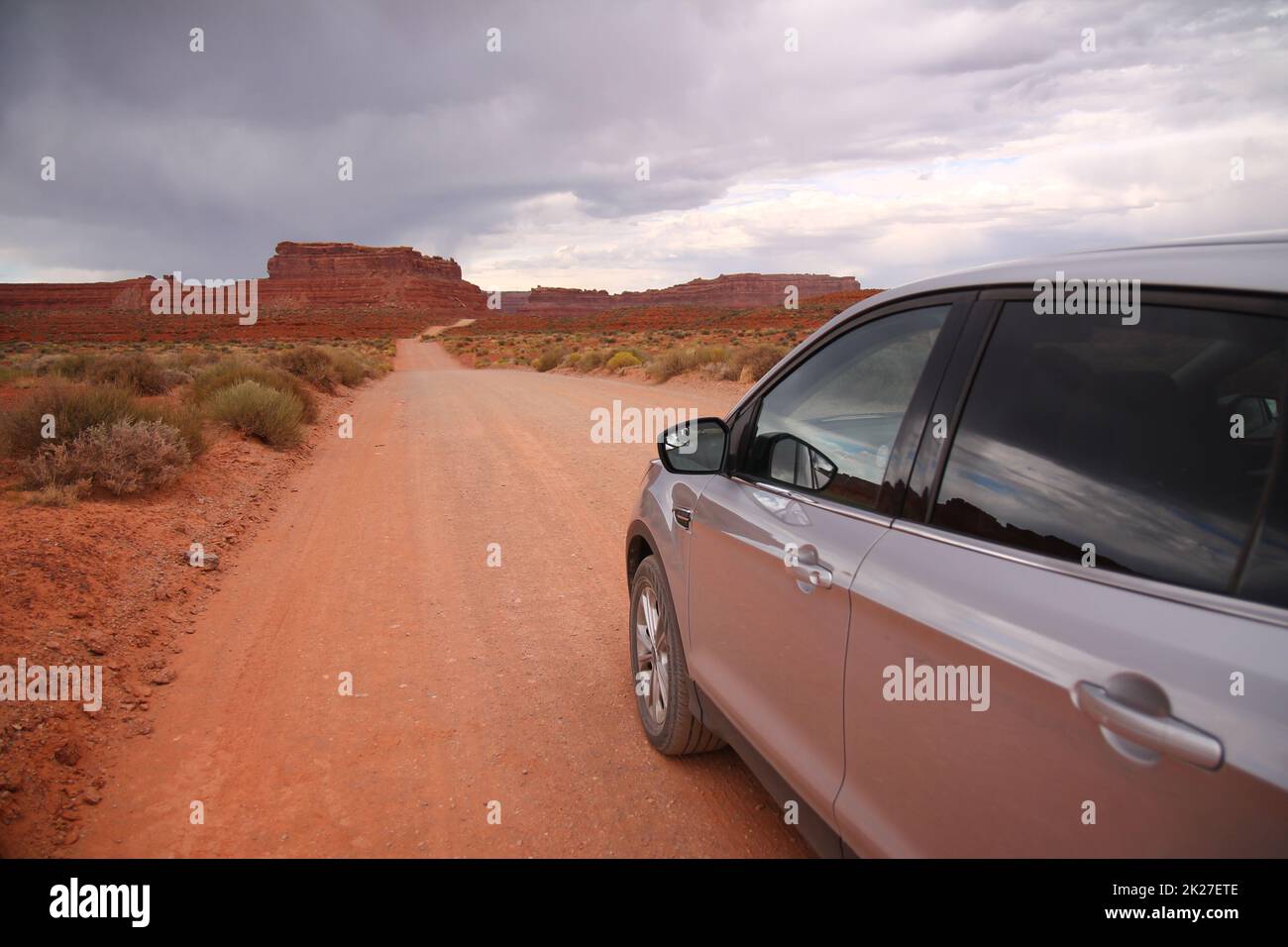 Una macchina grigia pronta per attraversare la strada di ghiaia rossa nella Valle degli dei Foto Stock