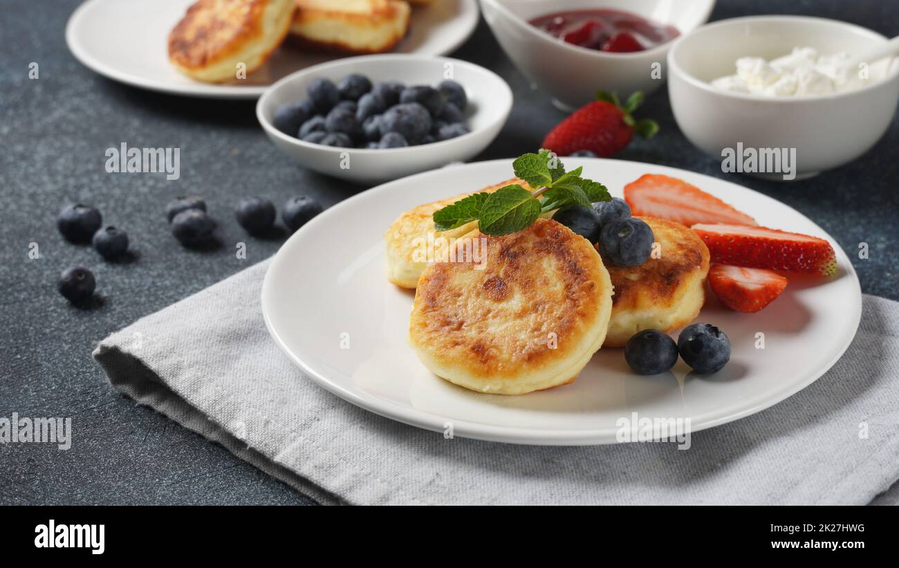 Frittelle di formaggio caserma o sciroppi o frittelle con mirtilli freschi, fragole e confettura di fragole. Gustoso dessert o colazione dolce. Russo, cucina Ucraina Foto Stock