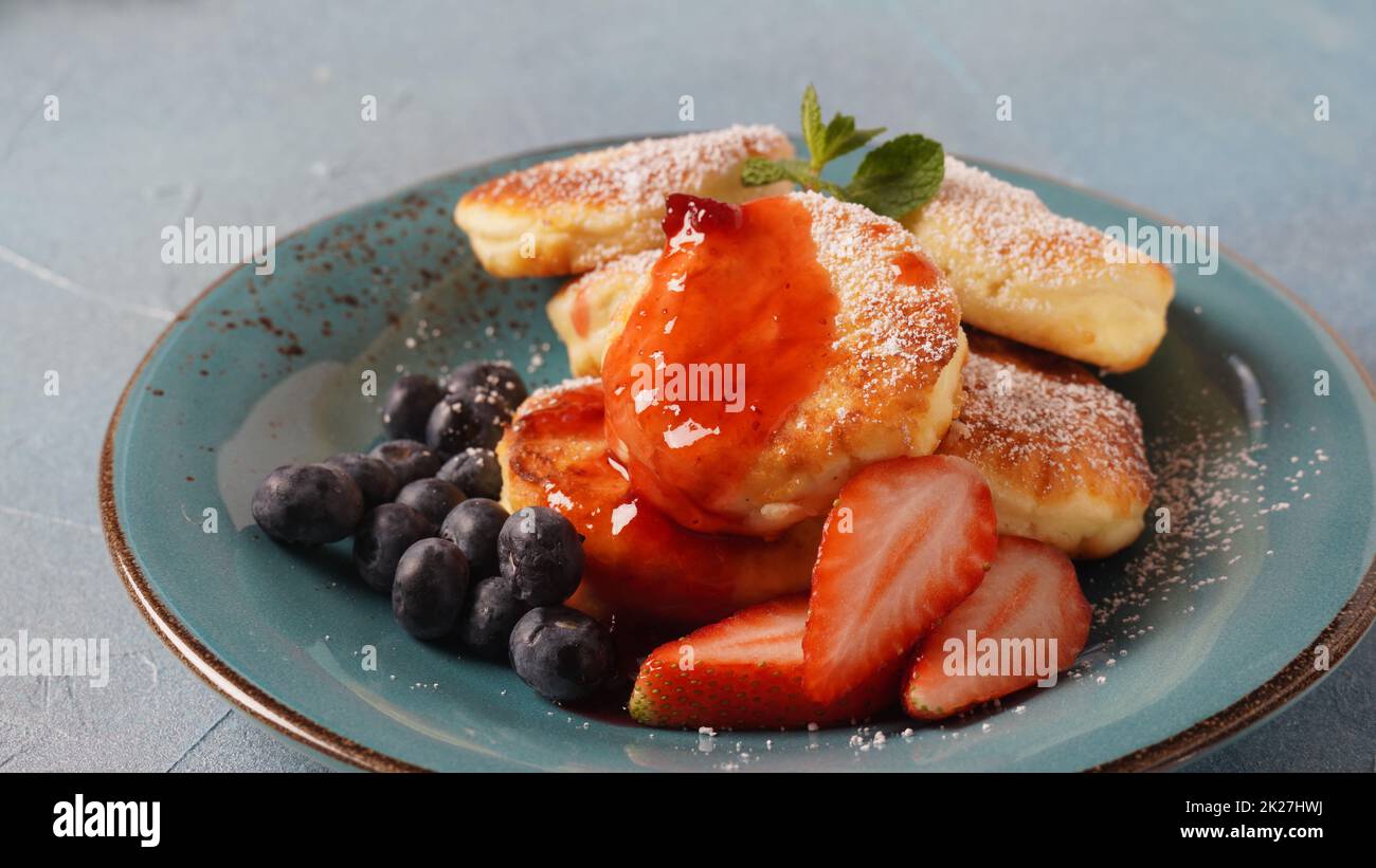 Frittelle di formaggio caserma o sciroppi o frittelle con mirtilli freschi, fragole e confettura di fragole. Gustoso dessert o colazione dolce. Russo, cucina Ucraina Foto Stock