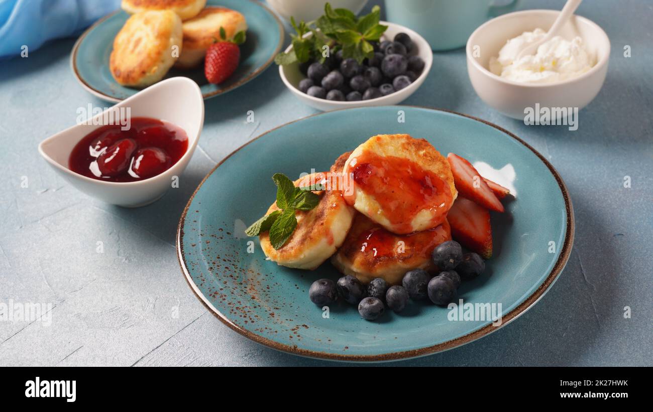 Frittelle di formaggio caserma o sciroppi o frittelle con mirtilli freschi, fragole e confettura di fragole. Gustoso dessert o colazione dolce. Russo, cucina Ucraina Foto Stock