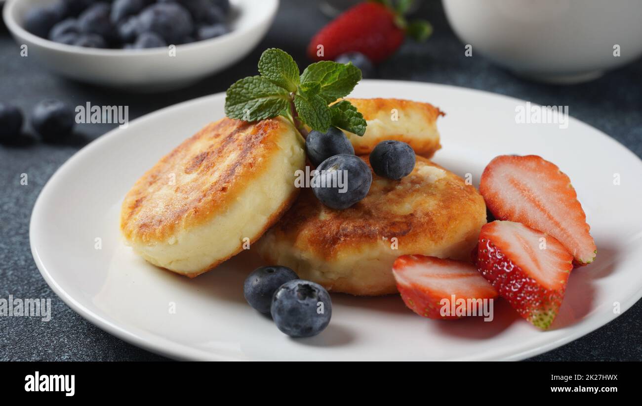 Frittelle di formaggio caserma o sciroppi o frittelle con mirtilli freschi, fragole e confettura di fragole. Gustoso dessert o colazione dolce. Russo, cucina Ucraina Foto Stock