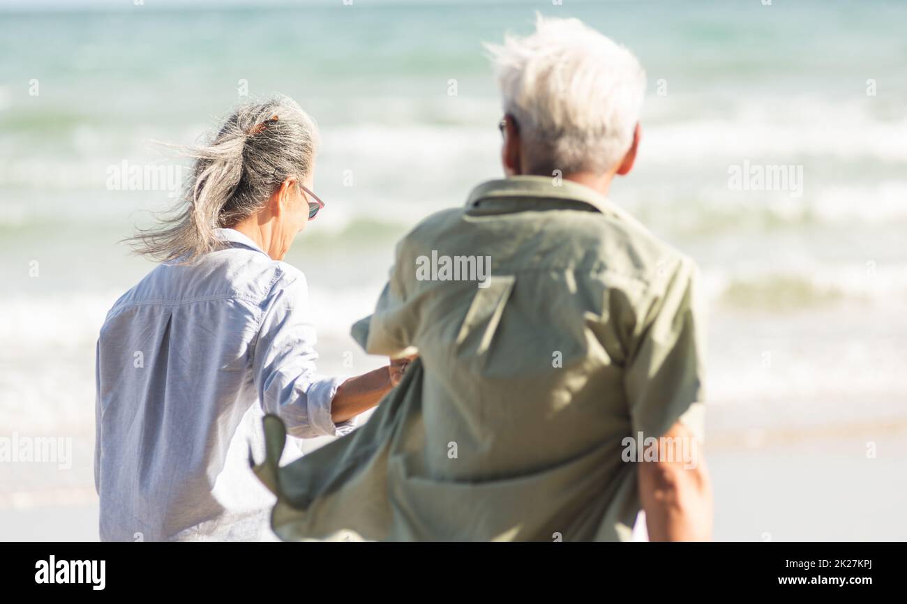 coppia uomo e donna senior che tiene le mani a piedi fino alla spiaggia soleggiata con cielo blu brillante Foto Stock