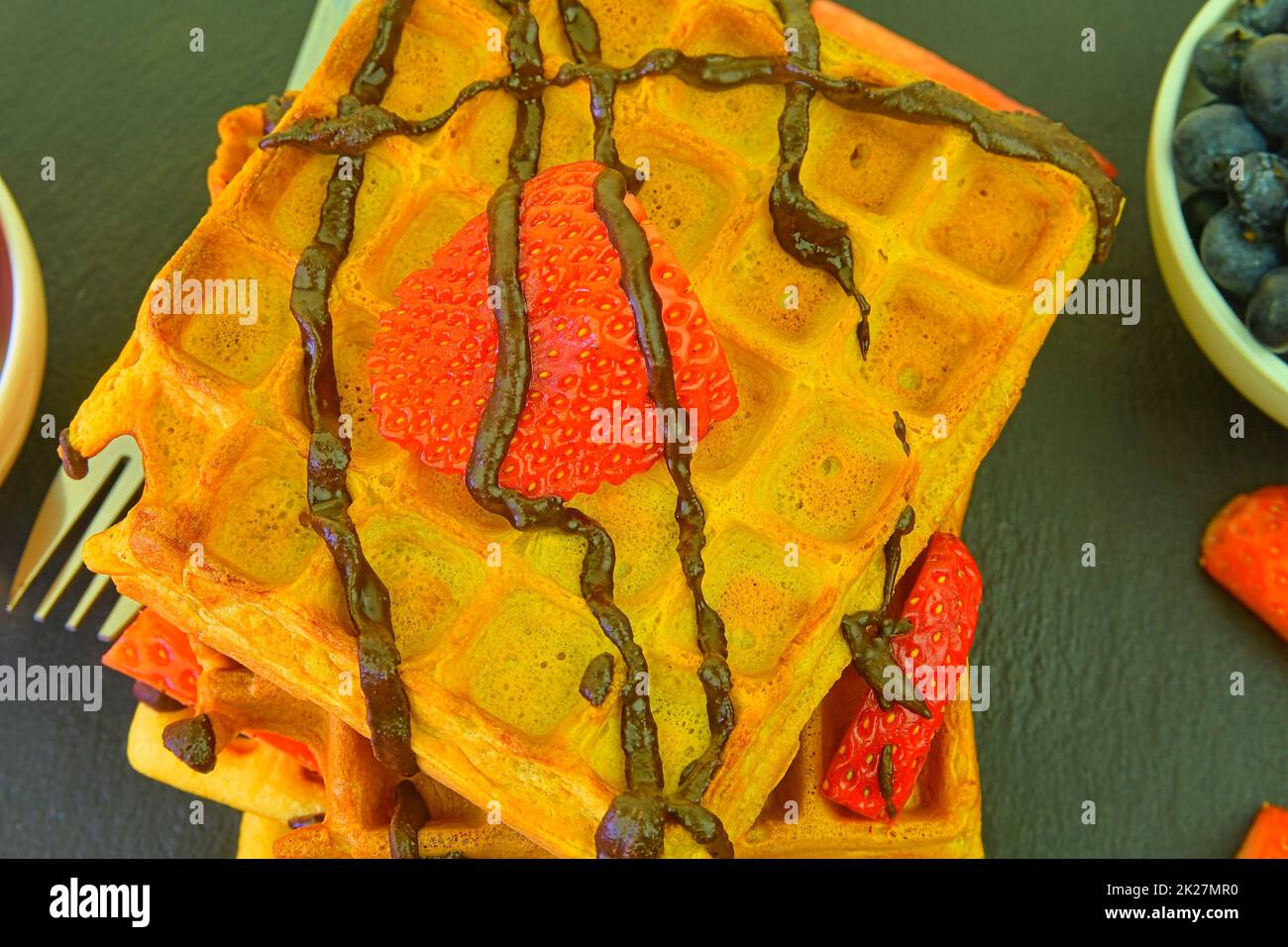 Waffle belgi fatti in casa con mirtilli e fragole su sfondo ardesia. Cioccolato fuso su cialde. Design piatto Foto Stock
