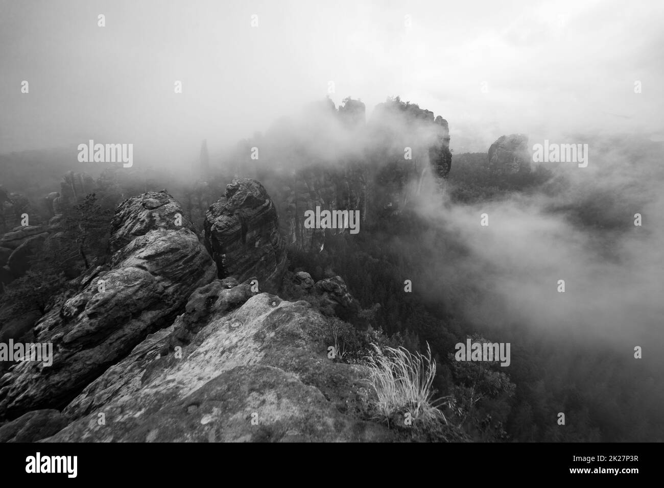 Una mattina presto nuvolosa in montagna. Schrammsteine - un gruppo di rocce è un lungo, steso-fuori, molto frastagliato nelle montagne di arenaria dell'Elba situato nella Svizzera Sassone nella Germania orientale. Bianco e nero. Foto Stock