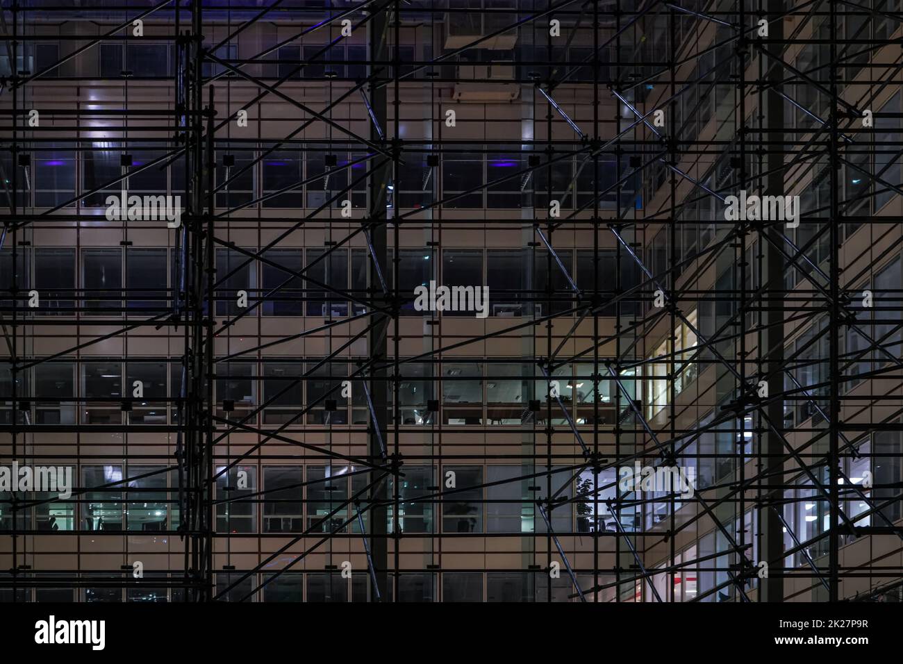 Costruzione di ponteggi in ferro attorno a un moderno edificio in acciaio e vetro per uffici di notte Foto Stock