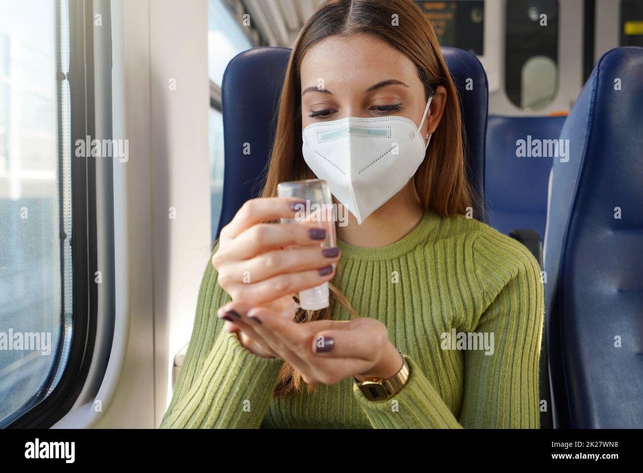Donna d'affari in treno con maschera facciale obbligatoria utilizzando alcool gel sanitizzante mani. Concetto antisettico, igienico e sanitario. Foto Stock